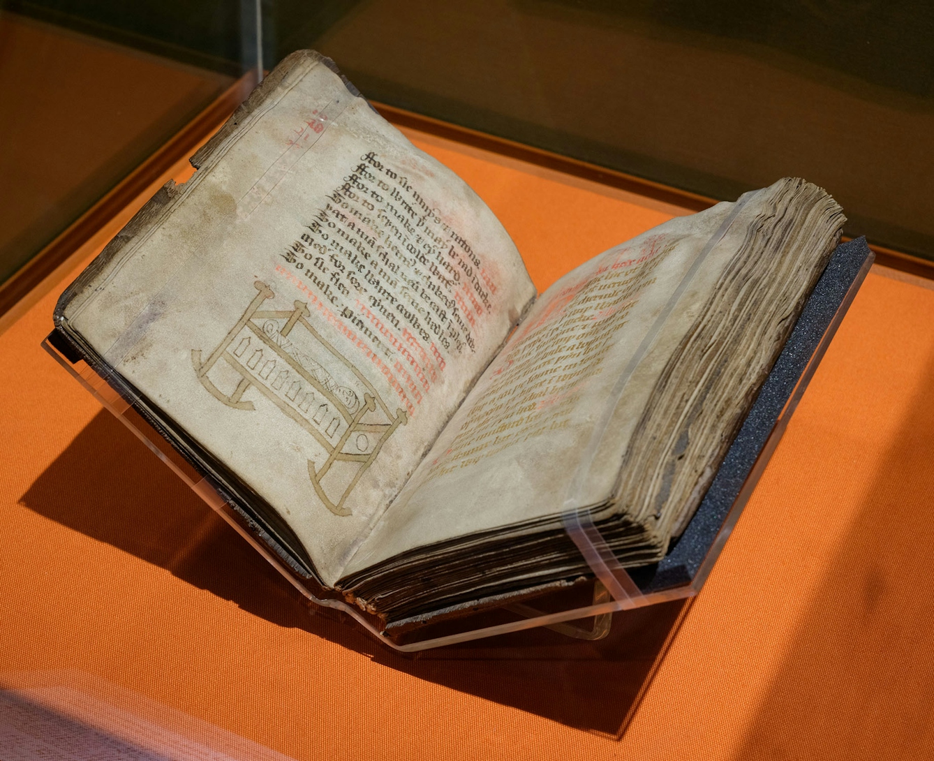 An open book on display in an exhibition. The page on the left shows hand-written text and a drawing of a swaddled baby in a rocking cot.