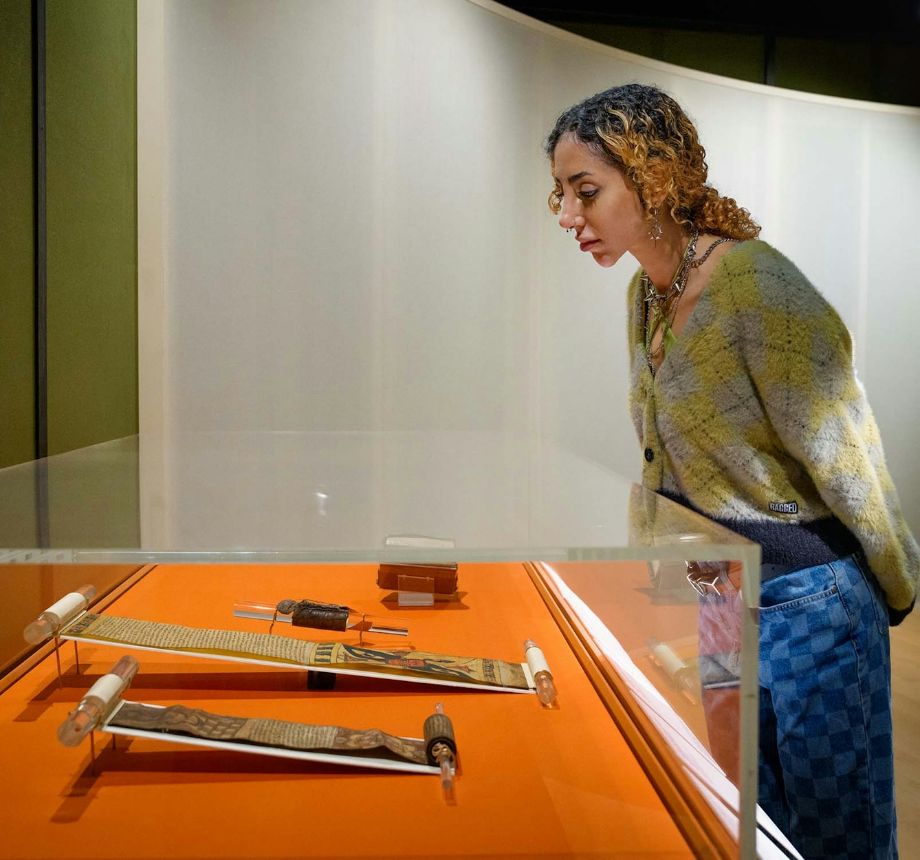 A young woman leans forward to look at objects in a glass display case in an exhibition gallery.