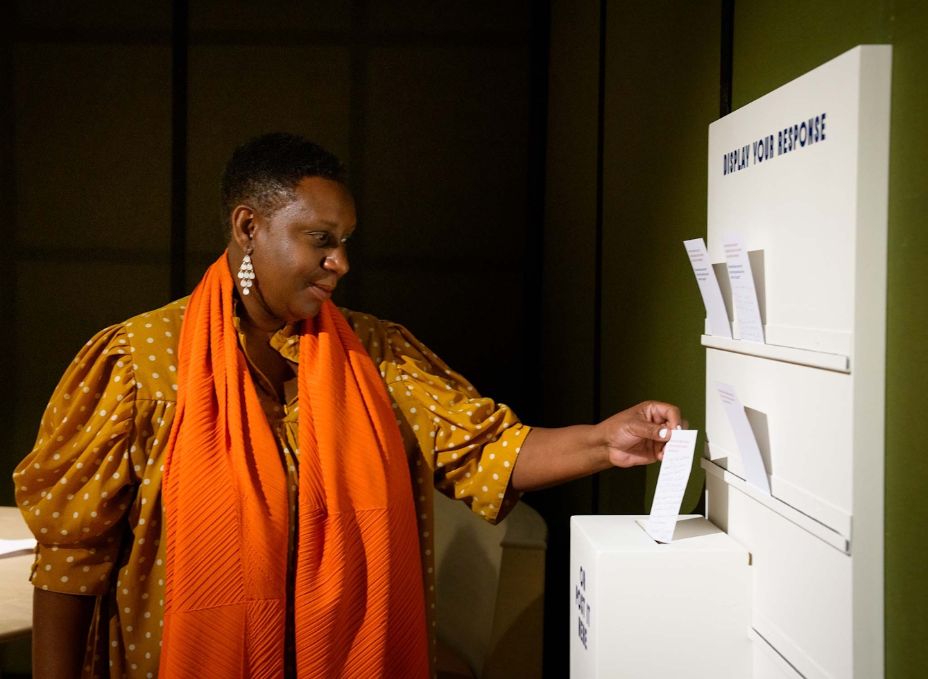 A woman holds a comment card in front of a rack of other cards. 