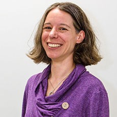 Headshot of Maria wearing a bright purple top, smiling into the camera