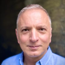 A black and white photograph of the head and shoulders of a middle-aged man with grey hair. He is smiling and looking directly at the camera.