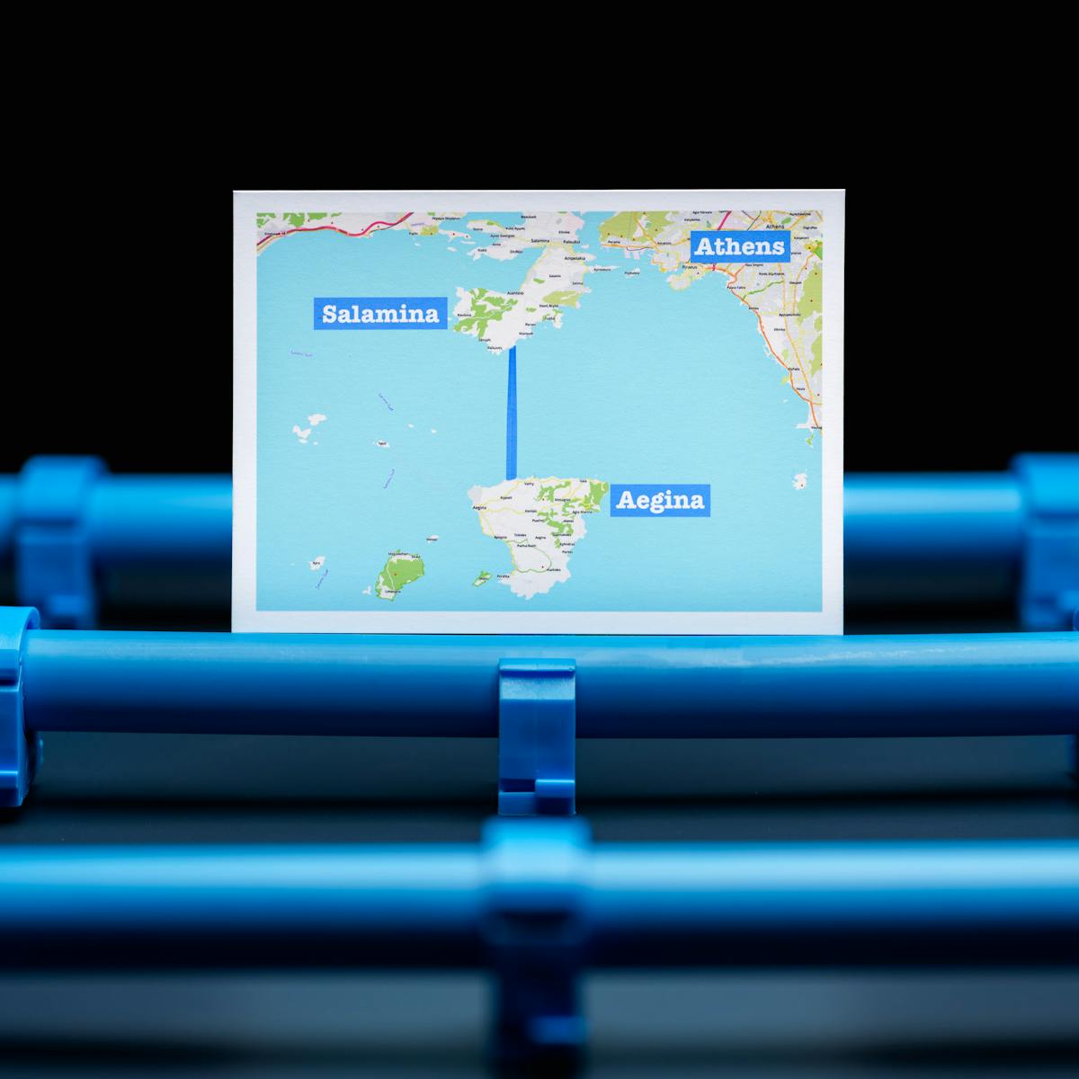 A map showing the pipe connection between the Greek Islands Salamina and Aegina. The map is positioned on a background of blue water pipes.
