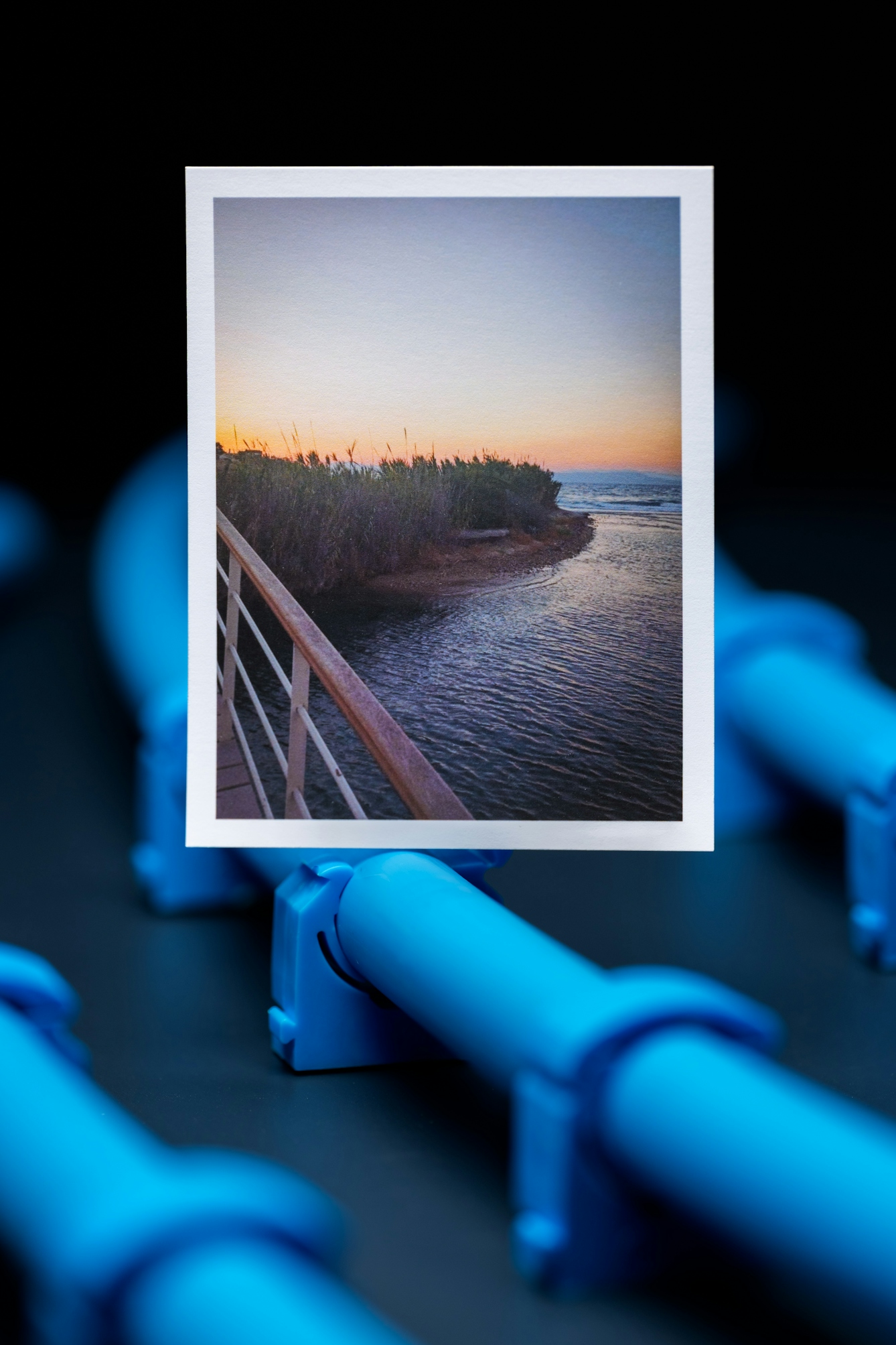 A photograph of a coastal scene at sunset. The photograph is positioned on a background of blue water pipes.