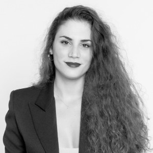 Black-and-white head-and-shoulders portrait of a woman with long, wavy hair, wearing a dark blazer over a light top, looking at the camera with a slight smile.