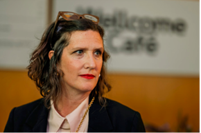 Head and shoulder photo of Laurie Britton Newell, a person with brown hair wearing a black blazer and white collared shirt. They are looking to their left.