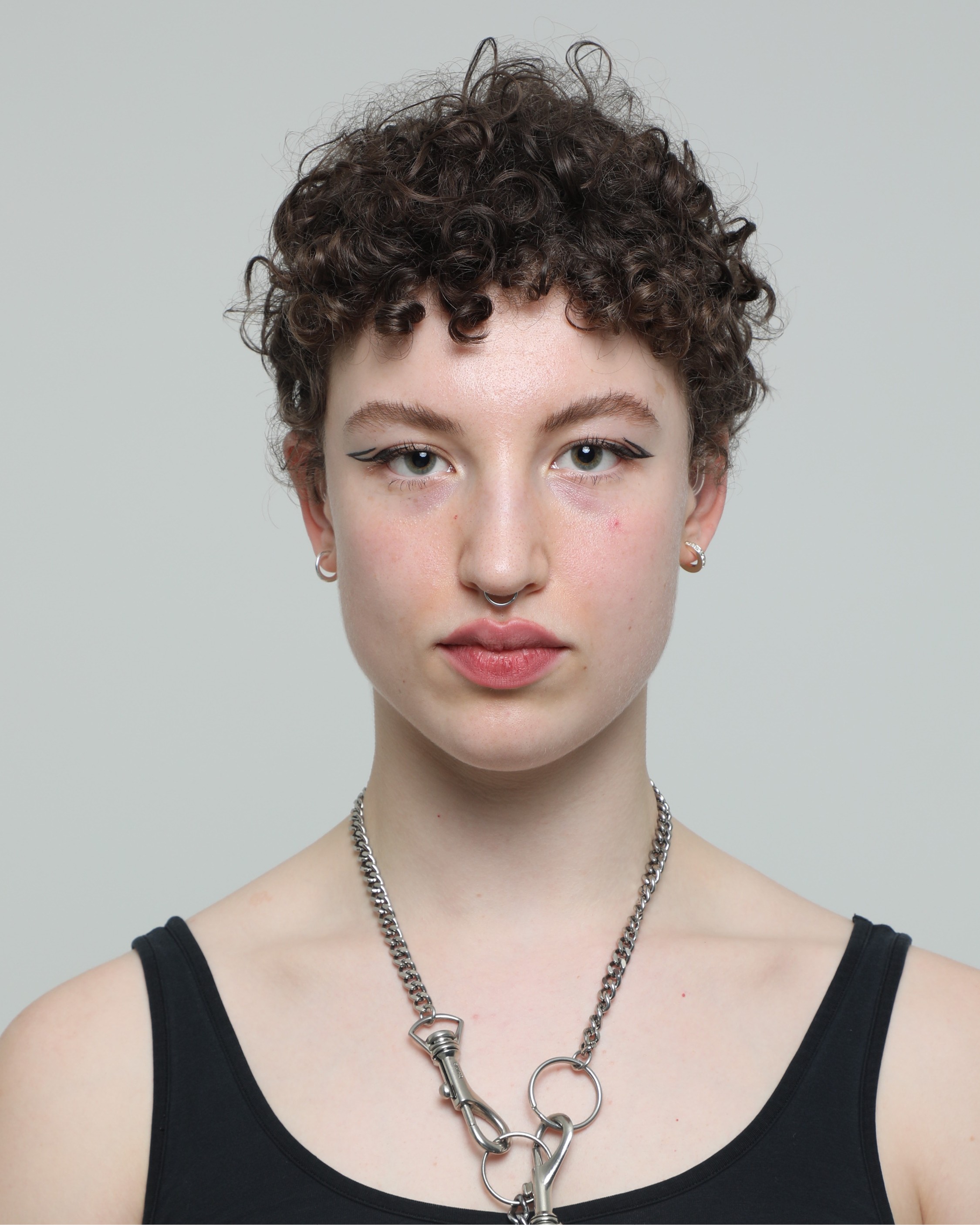 Headshot of Mirabelle Haddon, a person with short curly hair wearing a black vest. They are looking to camera.