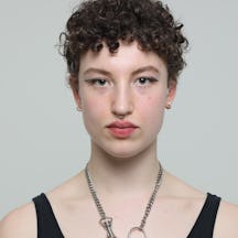 Headshot of Mirabelle Haddon, a person with short curly hair wearing a black vest. They are looking to camera.