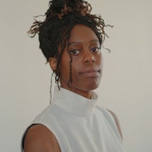 Photo of Temitope Ajose, a person with dark hair in a high bun, wearing a white high-neck vest. They are looking to camera, with their body angled to the side.