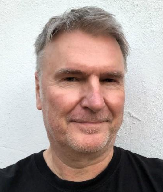 A headshot photo of a man with grey hair wearing a black top