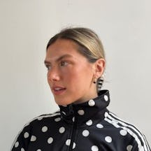Lotte is blonde with hair clipped back in a bun, wearing a polkadot zip-up jacket with stripes on the shoulders.