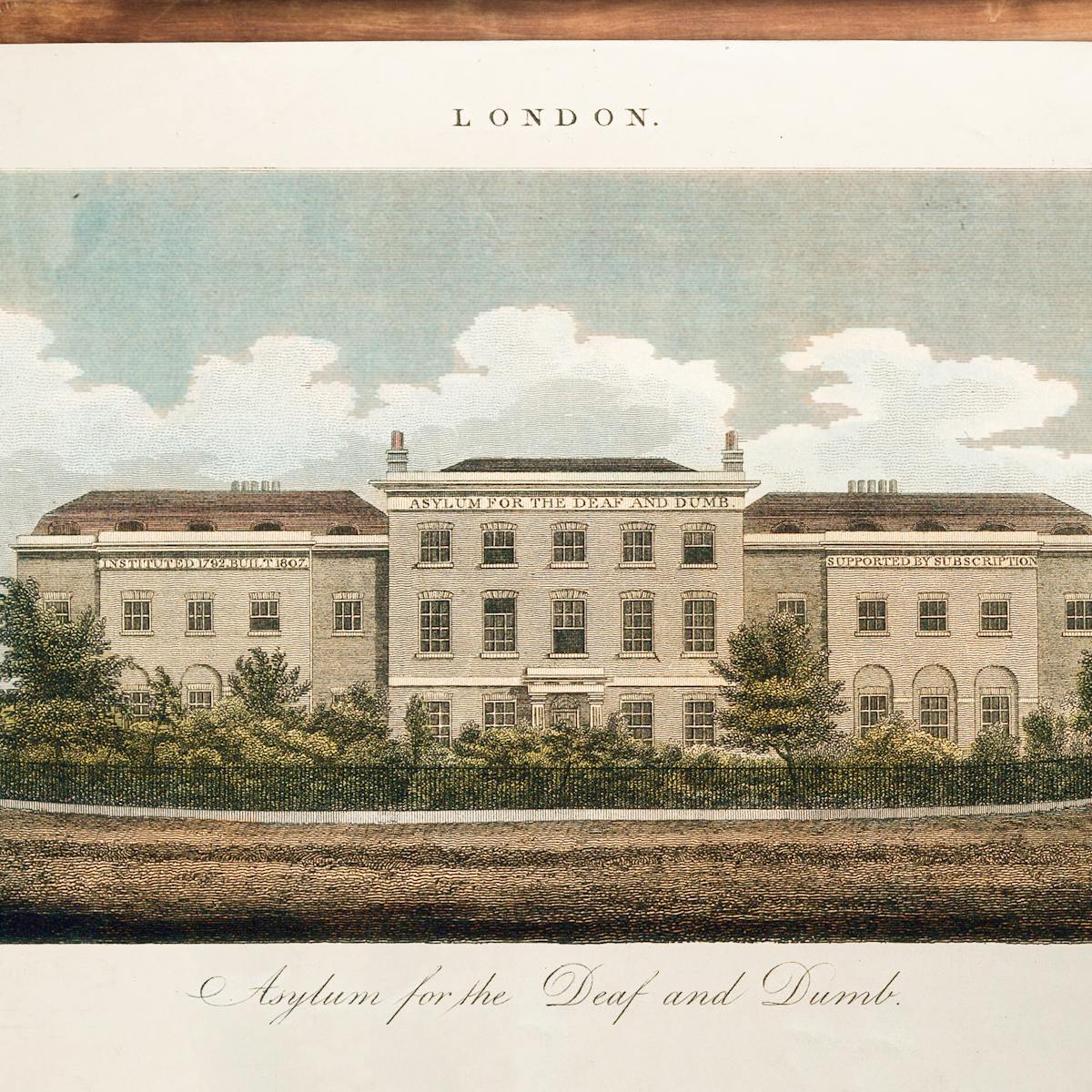 Wooden tabletop on which rests a colour engraving of a large 19th century stone building. Lettering on the front of the building reads "Asylum for the Deaf and Dumb."