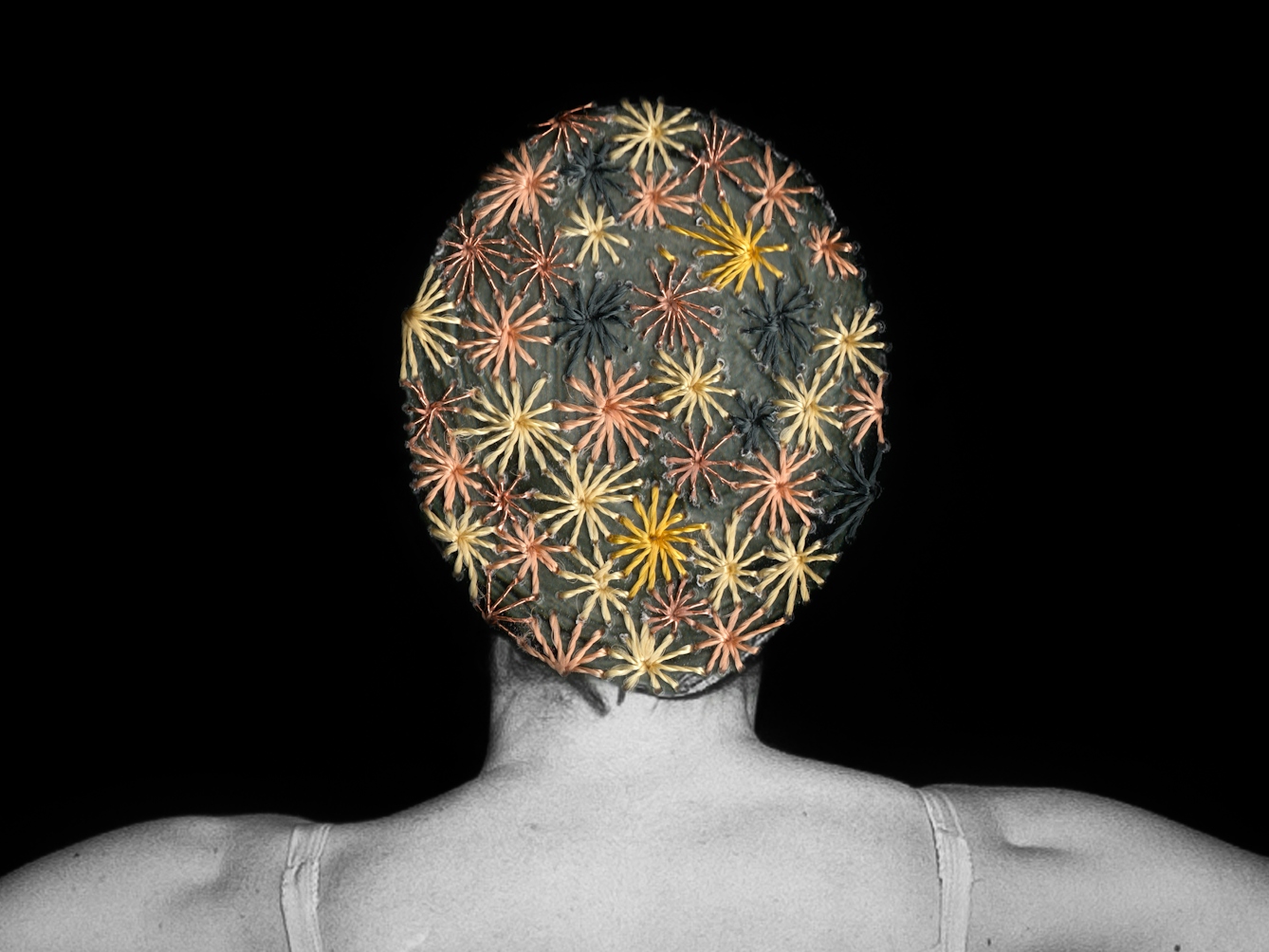 Artwork made up of a black and white photograph of a female figure from behind, from the waist up, against a black background. Embroidered into the photographic print with yellow and orange coloured thread is a crisscross floral pattern which exactly covers her head and hair.