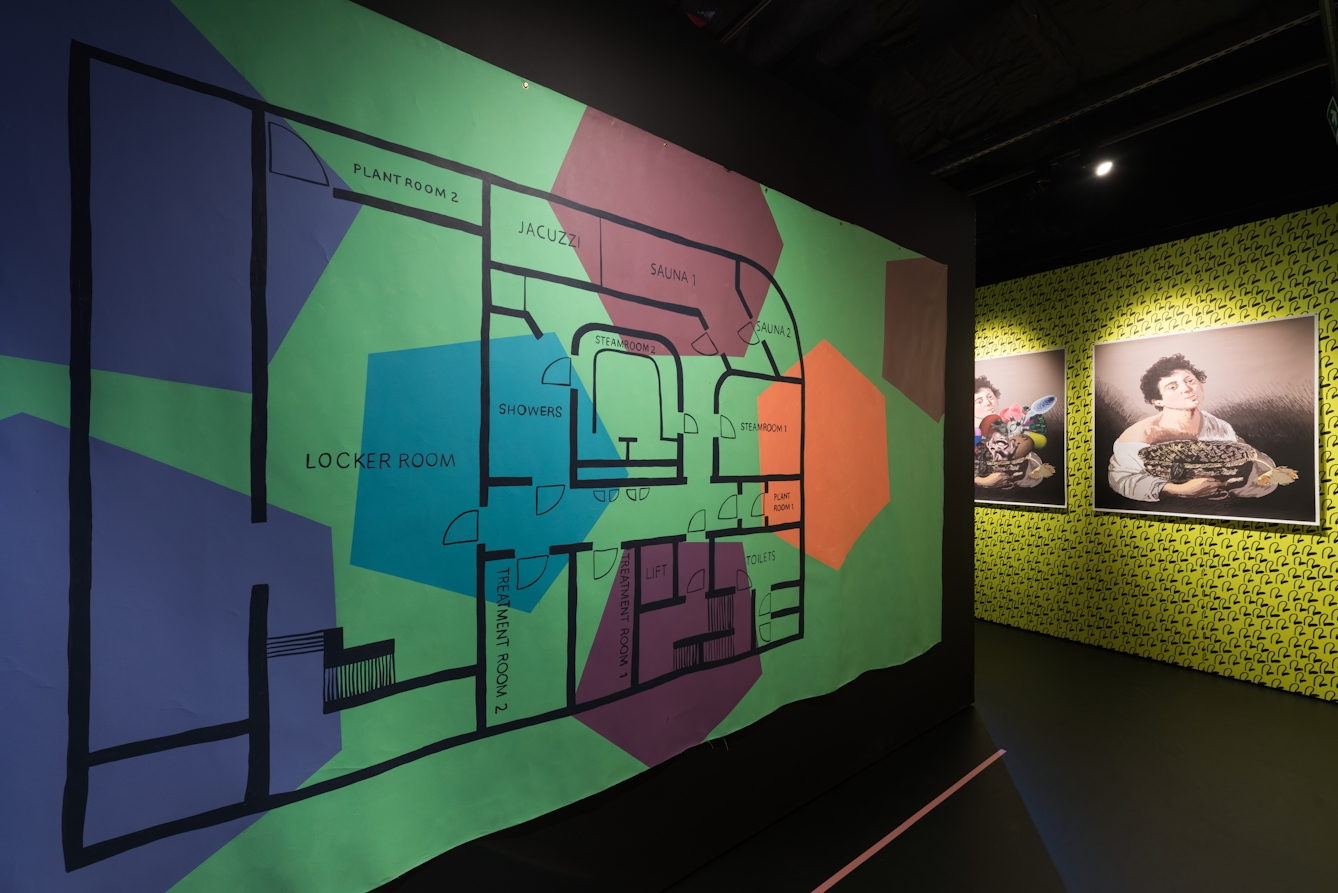 Photograph of gallery installation showing a large floor plan hung on the wall.