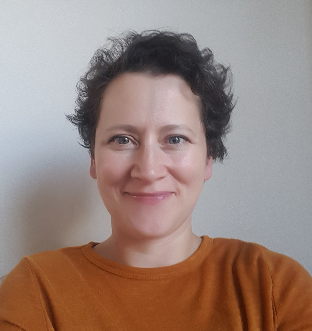 Black and white photograph of a the head and shoulders of a young woman with short dark hair. She is smiling and looking directly at the camera.