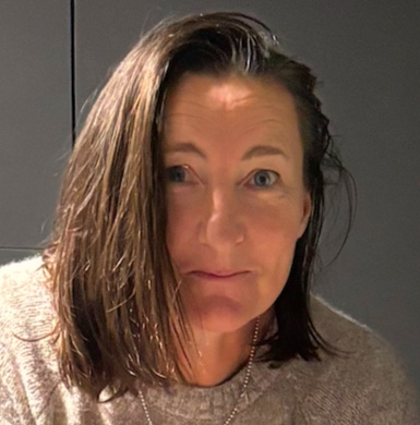 Photograph of the head and shoulders of a woman with dark shoulder-length hair. She is smiling and looking at the camera.