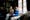 Photograph of a young woman and a mother figure in a domestic room. The young woman is seated in a long dress and and the mother figure sits beside her. The young woman is looking to the mother figure who is looking to camera.