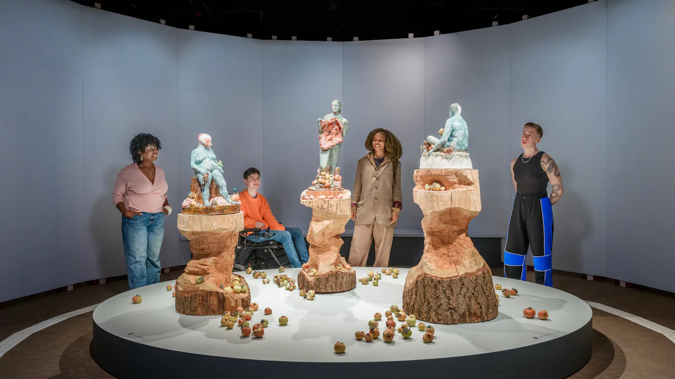 A group of visitors look at an installation that features three sculptures of women figures.