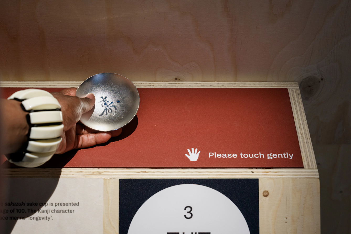 A visitor wearing a cream-coloured bracelet picks up a silver sake cup.