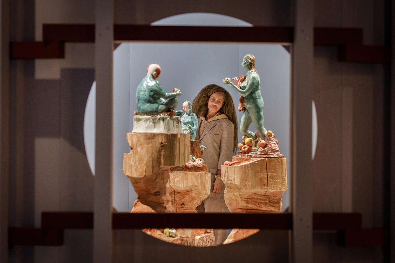 A visitor looks at an installation that features three sculptures of women figures. They are framed by a circular cut-out in the wall.