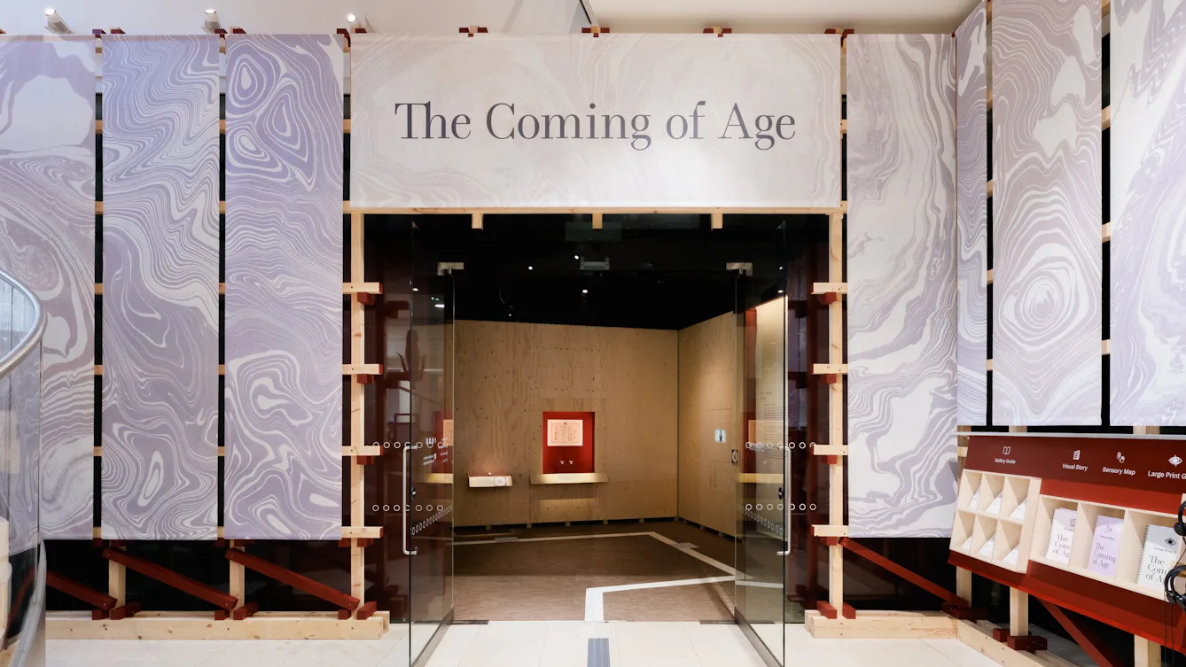 The atrium outside Gallery 1 at Wellcome Collection featuring a large sign above the doorway that reads 'The Coming of Age'.