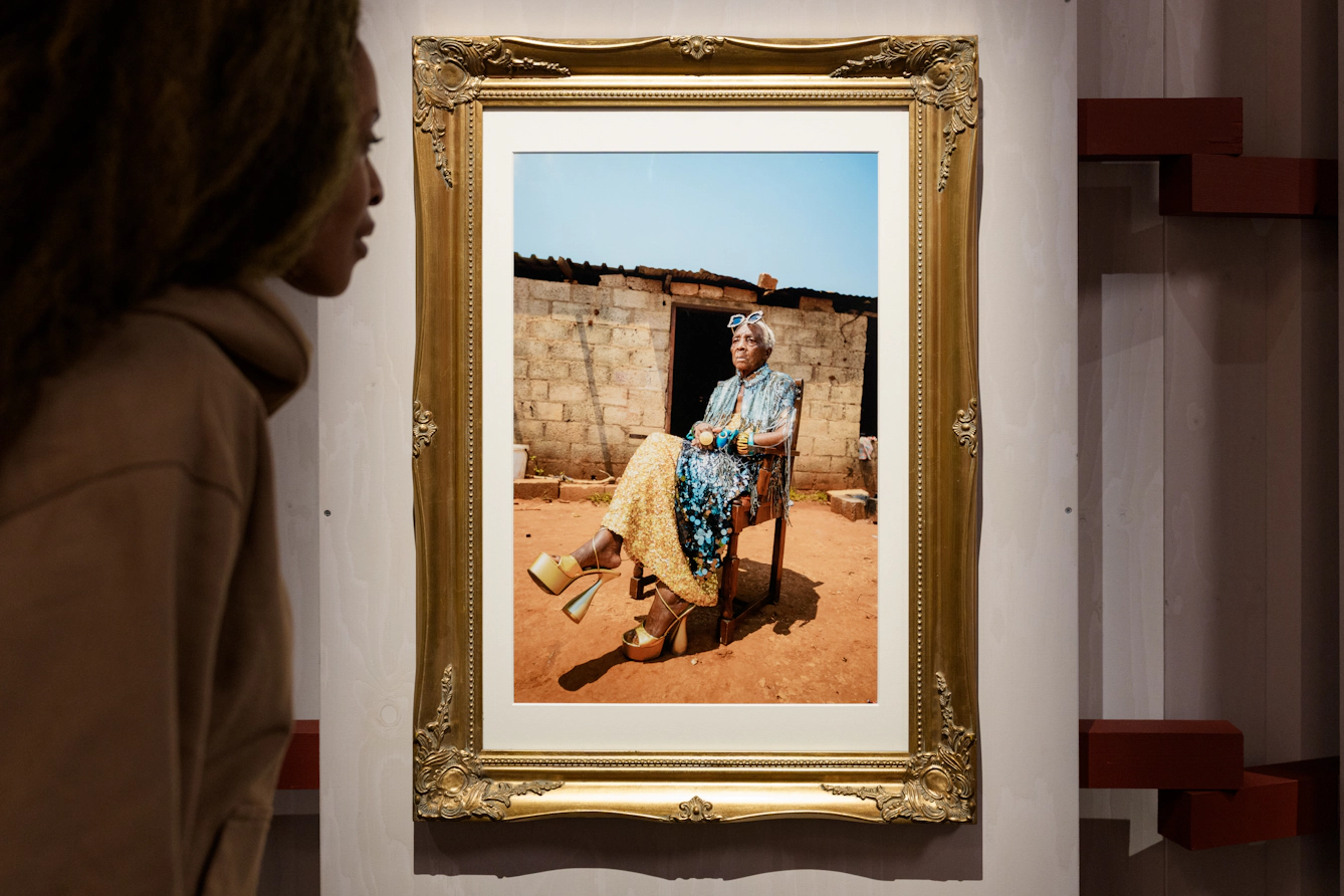 A visitor looks at a portrait of a grandmother in a rural African village, wearing colourful high-fashion clothes.