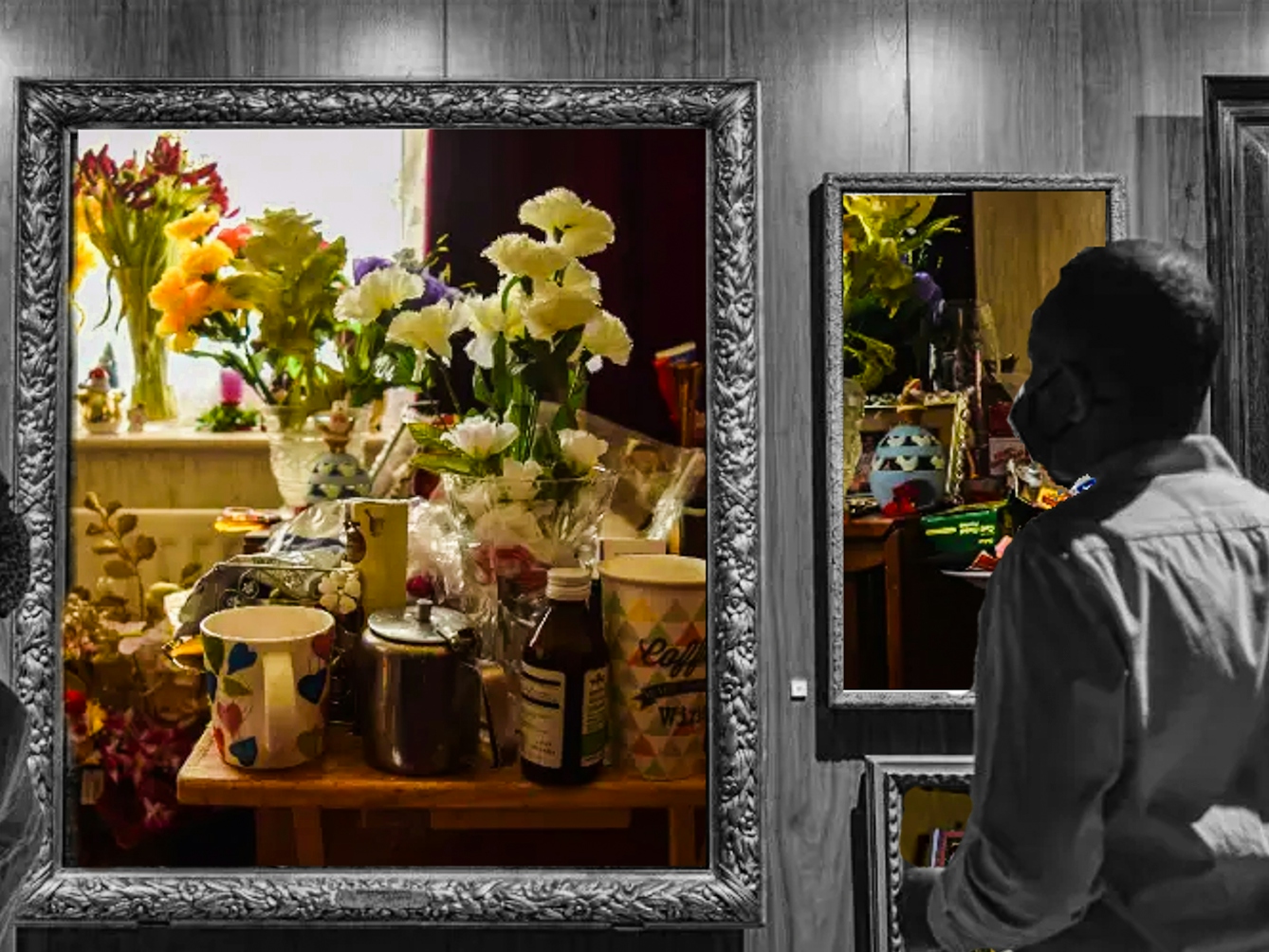 Crop of a black and white photograph showing a wall in a museum covered in large ornate picture frames. In the foreground are two people facing the wall of frames and wearing masks. Inside the black and white frames are colourful photographs showing different household objects. The largest frame in the center shows a table that has lots of things on top of it, all packed very close together, including vases of flowers, a mug and coffeepot, and medicine. On the windowsill behind the table are more flowers. The frame to the right shows a photo of a an equally crowded table, holding photo frames, flowers and various other trinkets.