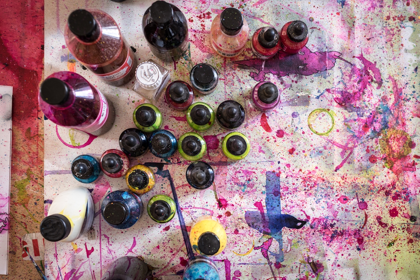 Photograph from above of colourful inks on a paint spattered drawing board.