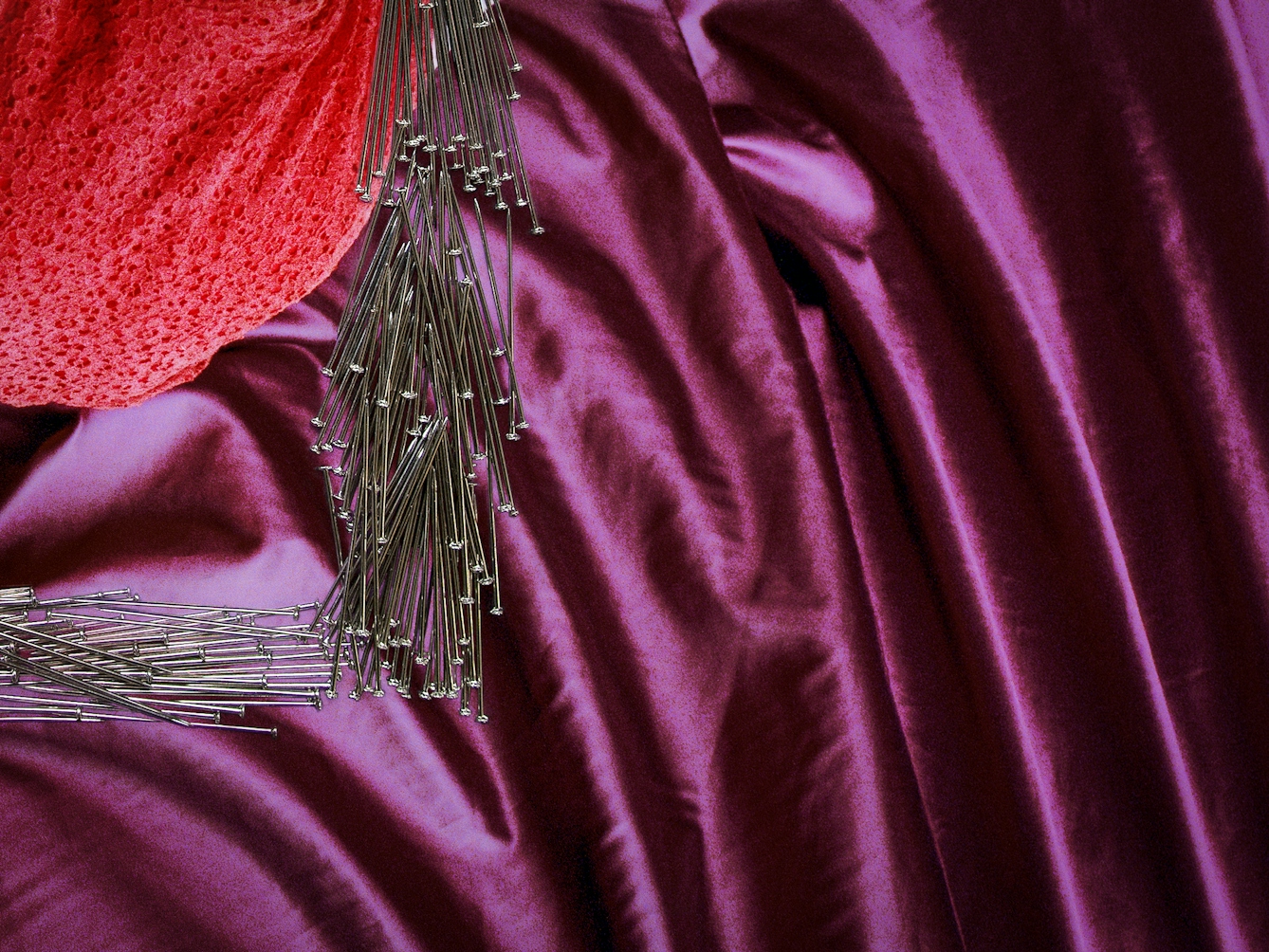 Detail from a larger artwork created with a colour photographic print of a female figure in a bright red dress, set against a purple and blue draped silk background.  Her body is covered by groups of dress pins, laid on top of the photographic print. The pins are arranged in a square frame shape. 