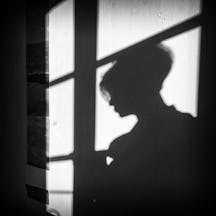 Photographic head and shoulders, back and white portrait of Debbie Loftus as a shadow against a wall.