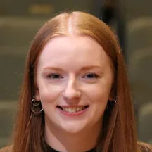 Black and white photograph of a young woman with long straight hair. She is smiling and looking directly at the camera.