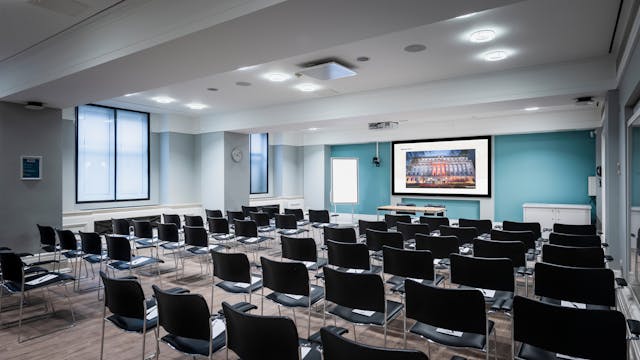 Photograph of the Franks and Steel room at the Wellcome Collection. 

Photograph shows a theatre space with chairs and a projector and screen set-up. There are large windows in the room. 