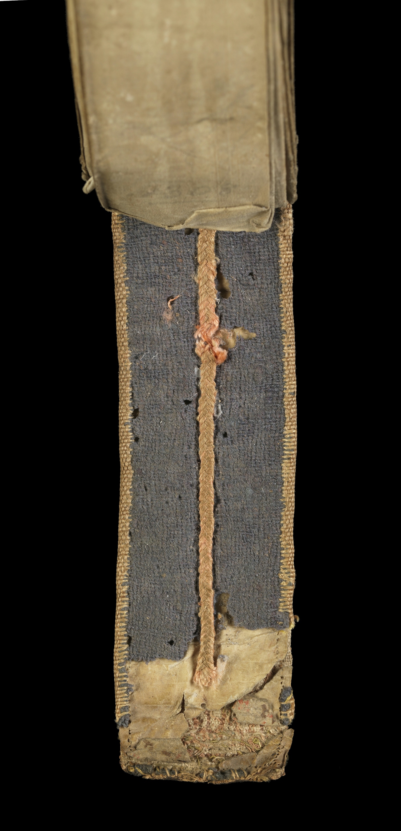 Photograph of a 15th century Medieval folding almanac. The embroidered binding is worn and there is an exposed layer of parchment below, with faint text lettering on it. 