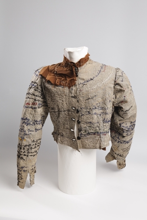 A photograph of a jacket on a mannequin. The garment, sewn by hand from coarse linen, is embroidered repeatedly with words in coloured thread – inside and out. 