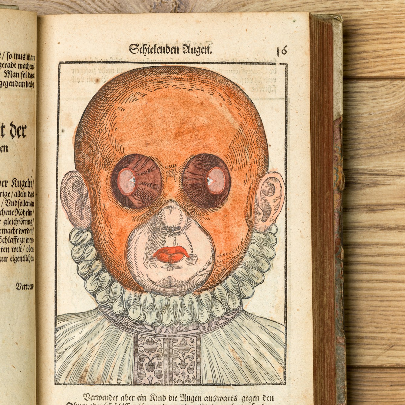 Photograph of an open book on a wooden background, showing a page with a coloured engraving from the 16th century depicting a person's head and neck ruff. On their head is a red mask which has small holes exposing the outside edges of their eyes and larger holes exposing their ears, nose and mouth.