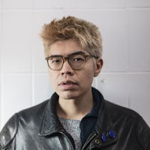 Photo of a man's head and shoulders. He is wearing glasses and a leather jacket and has dyed blonde hair