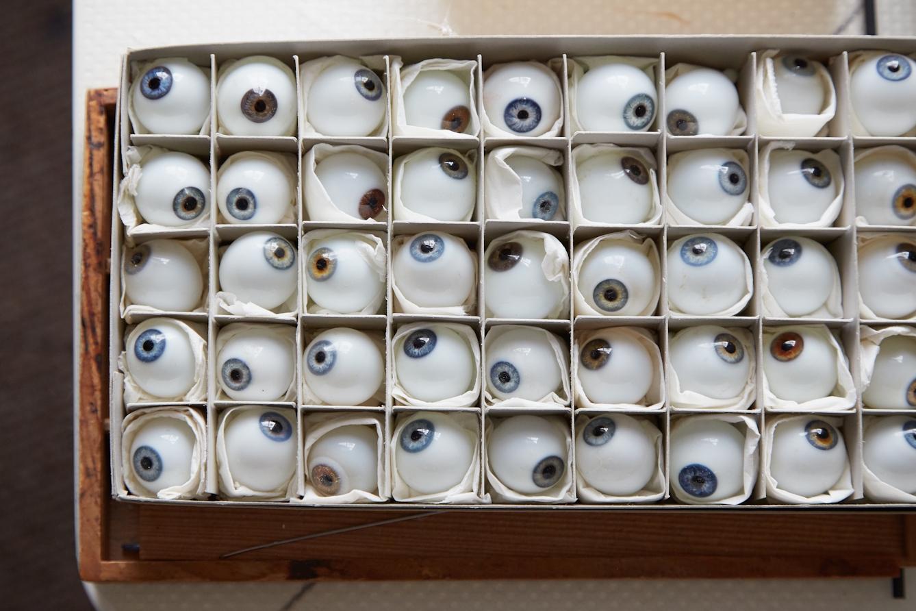 Photograph of a wooden box from above which is divided up into around 45 square partitions. In each partition is a glass eye with varying coloured irises.