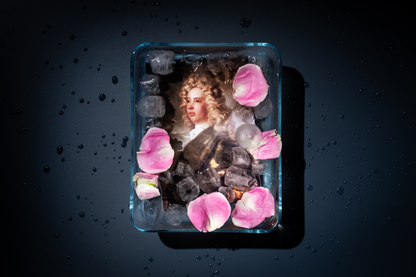 Photograph of a container filled with water, ice and flower petals. Through the water a portrait of the early 18th century Botanist Samuel Brewer.