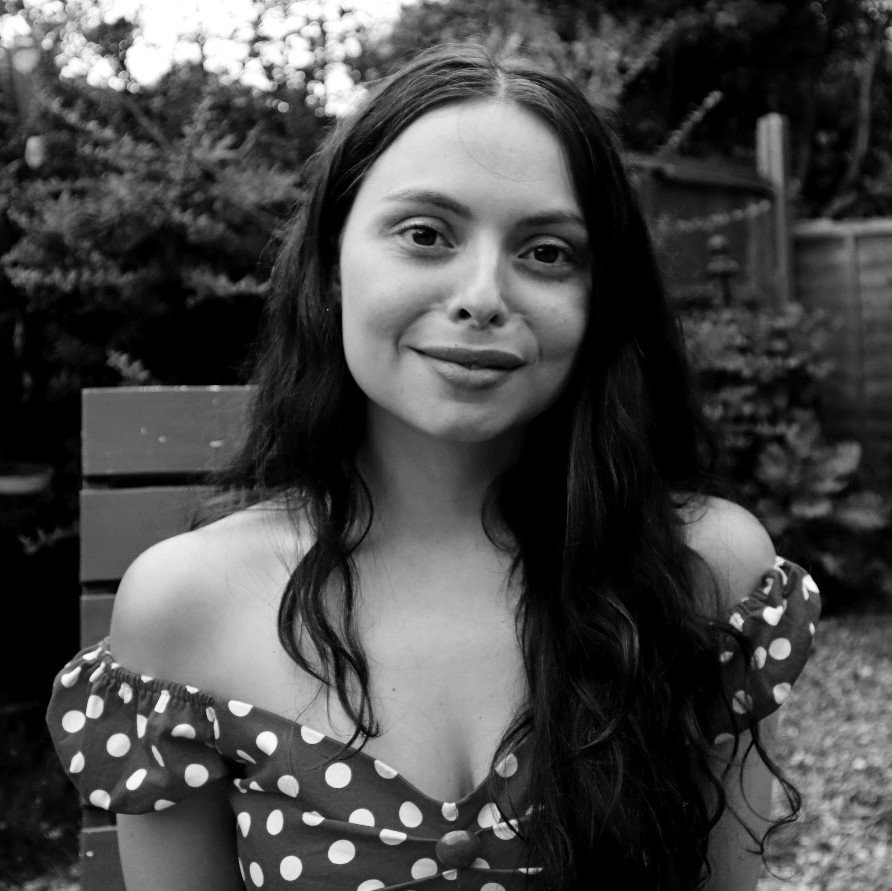 Black and white photograph of a the head and shoulders of a young woman with long dark hair. The woman is smiling and looking directly at the camera.