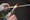 A hand in protective glove with thumb and forefinger cut away holds a glass rod above the flame of a blowtorch.