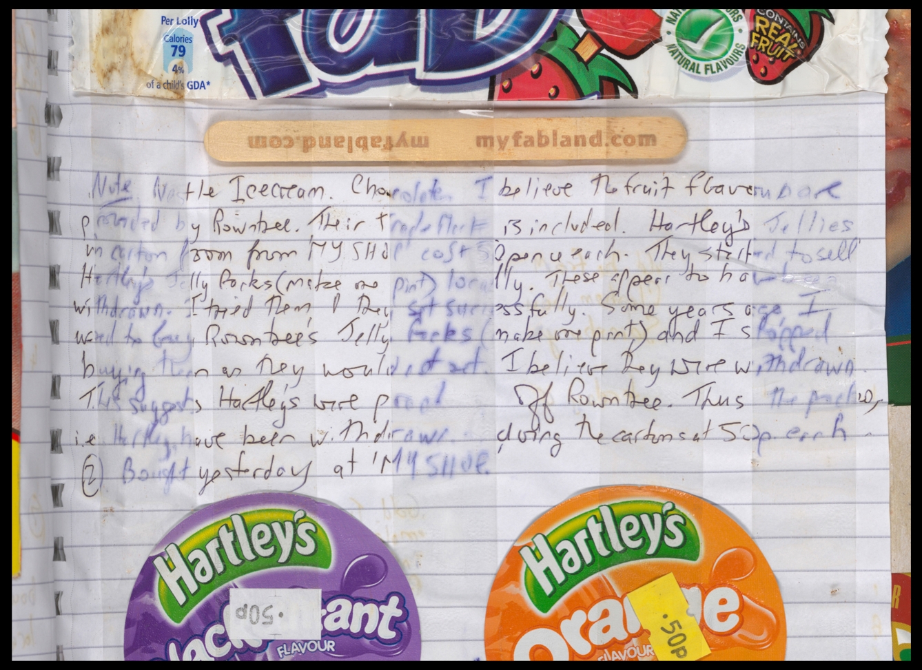 Photograph of a section of a page of a lined paper scrapbook. The page is covered in strips of Sellotape running vertically, which are holding in place an ice lolly wrapper, a wooden lollipop stick, the and lids of 2 jelly pots. In the centre of the image, between the wooden stick and the lids, are 10 lines of handwritten notes which talk about the items that have been stuck in. Where the tape intersected with the writing, the ink has bled into the paper and in some areas faded.