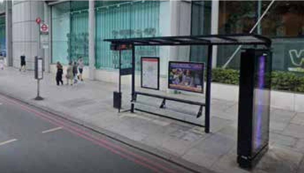 A steel and glass bus shelter and bus stop sign on a wide pavement in front of the Wellcome building on Euston Road London, UK.