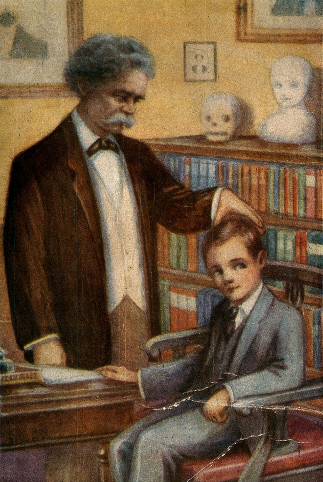 Colour image of a man standing up and a boy sitting down in a study. The man is touching the boy’s head, as if to gauge its width.