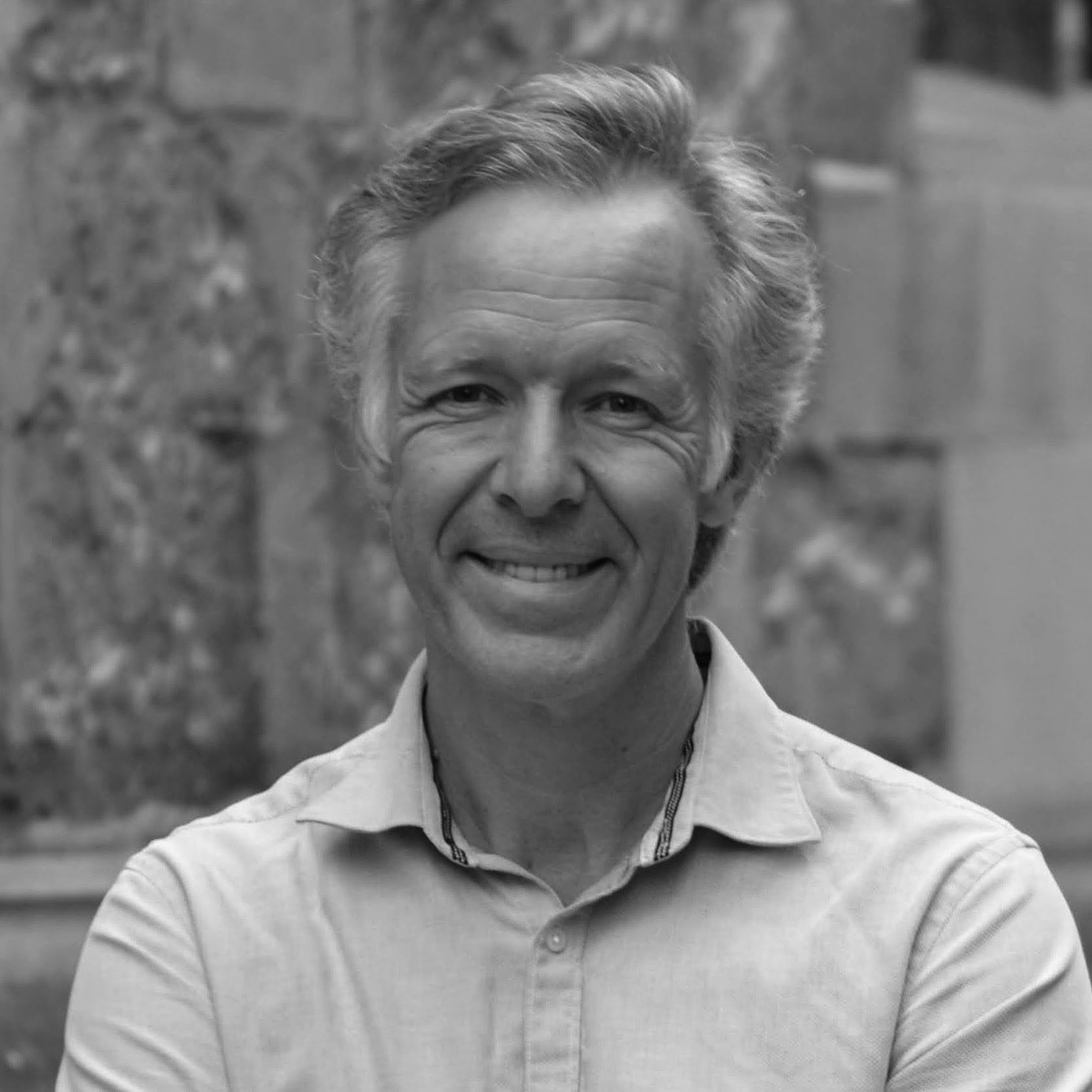 Black and white, head and shoulder photograph of a man with light hair wearing a pale shirt. The background is blurred.