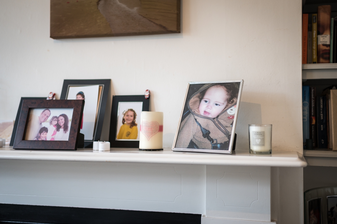 Photograph showing a mantlepiece with a collection of family photos in frames. The largest frame shows a baby in a fleece top.