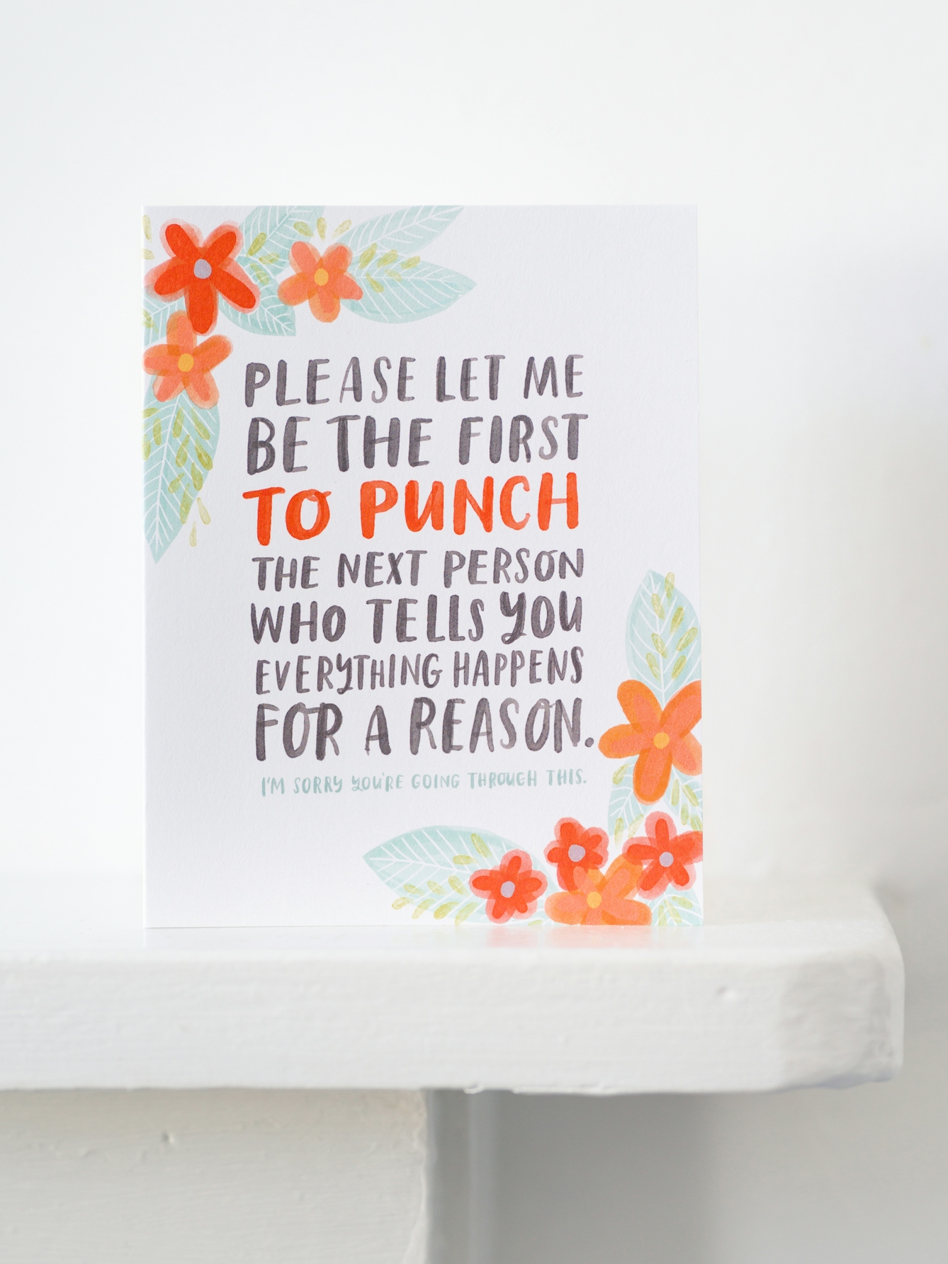 Photograph of a white mantelpiece against a white wall. On the mantlepiece is a greetings card which reads, 'Please let me be the first to punch the next person who tells you everything happens for a reason. I'm sorry you're going through this'.