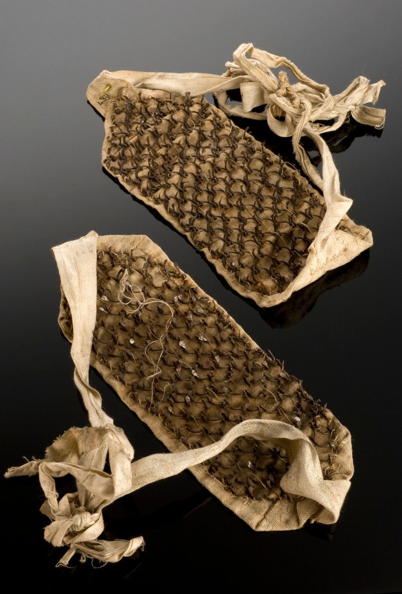 Image of brown rectangular patches of cloth with spikes on. Cloth bands attach at either end.