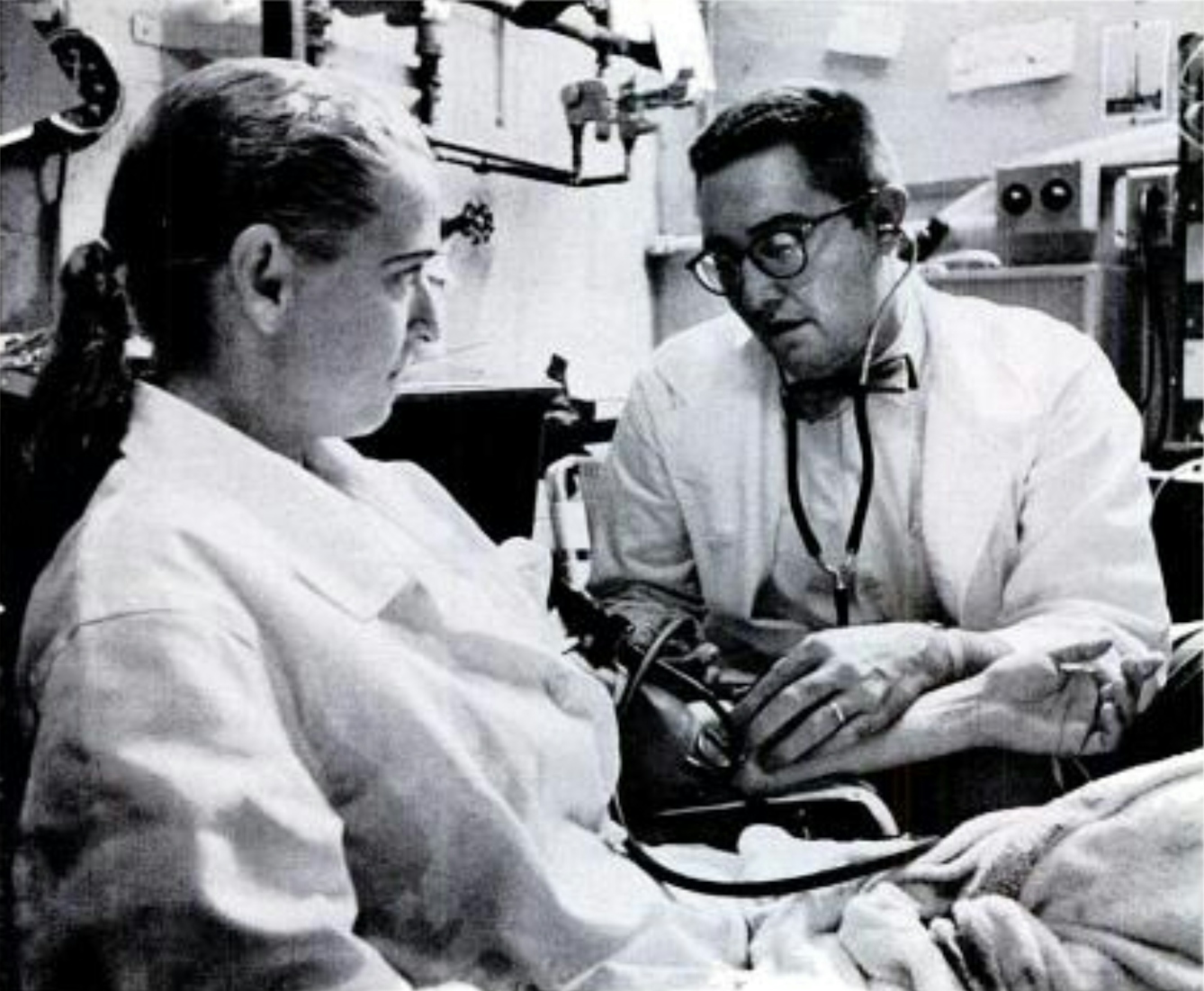 A man in a white coat examines a woman in a white coat.