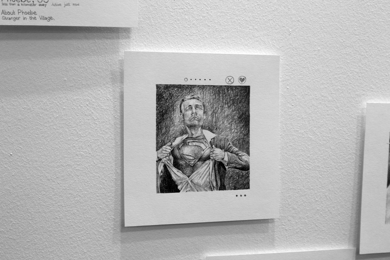 Photograph of an artwork in a gallery. The artwork is a pencil drawing of a man ripping open his shirt to reveal a Superman logo on his chest.