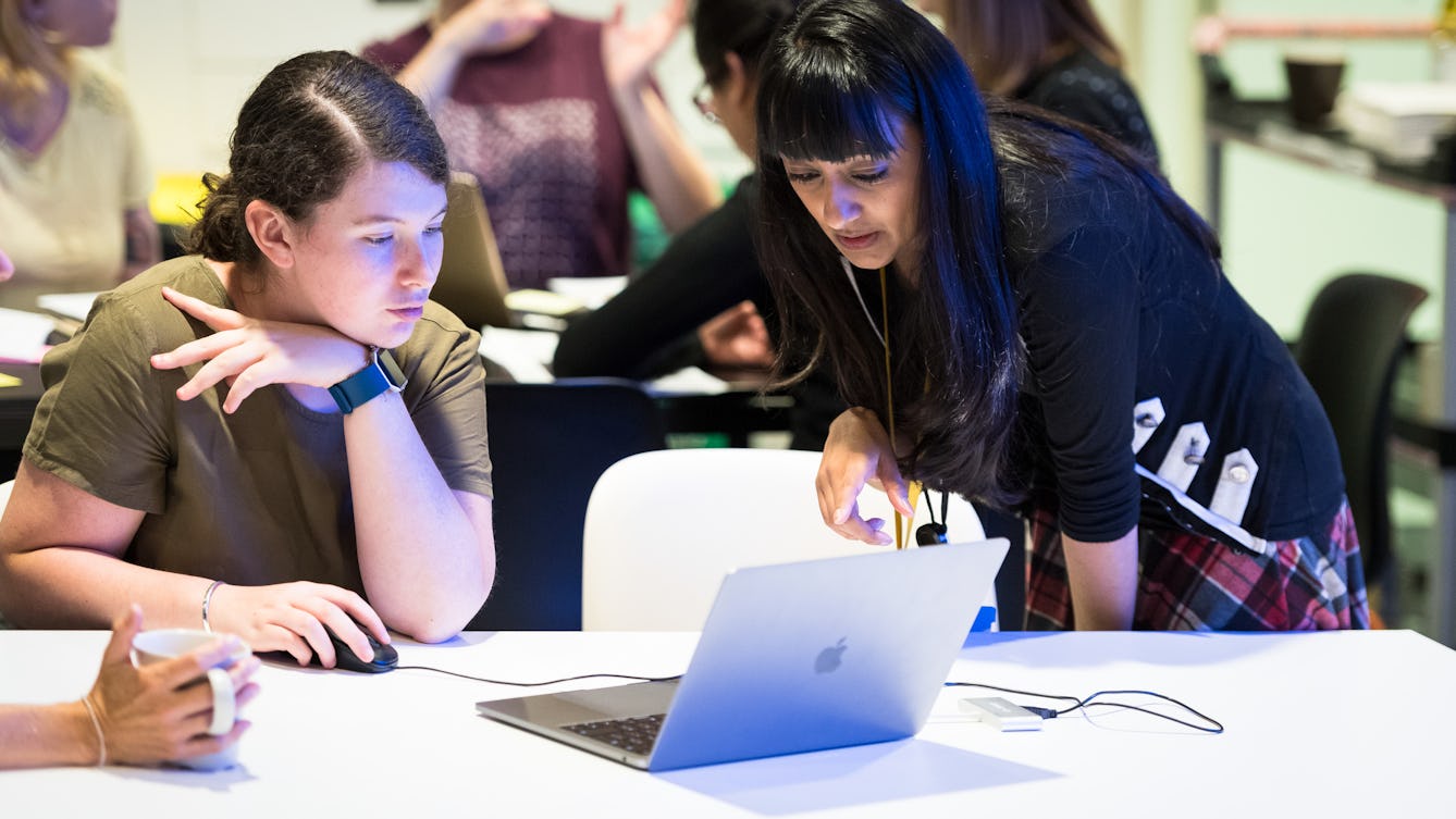 Photograph of a young woman working on a laptop computer in a class room environment whilst talking with a workshop facilitator.