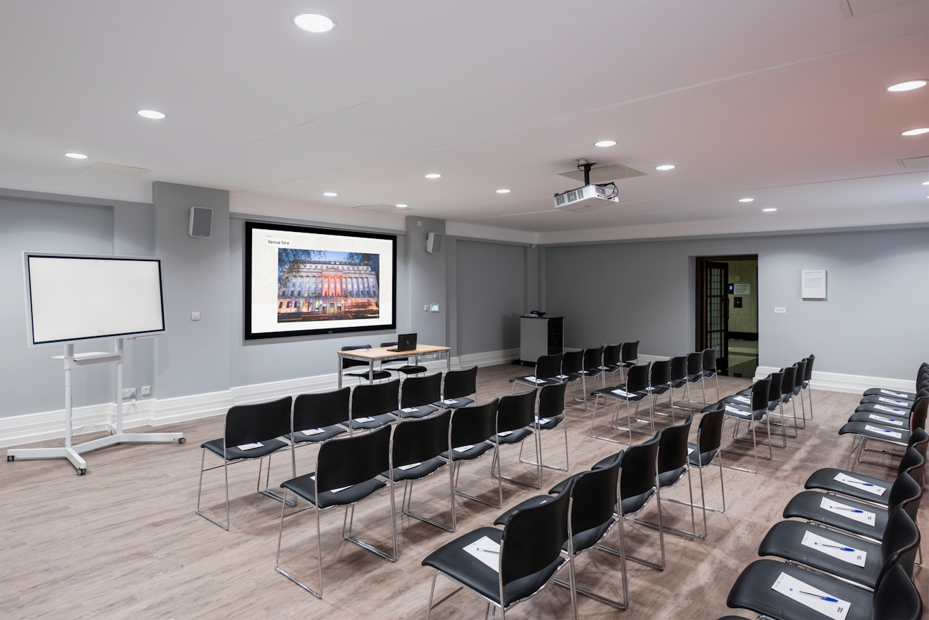 Photograph of the Burroughs room at the Wellcome Collection. 

Photograph shows a theatre set-up, with a presenting screen and whiteboard at the front of the room.